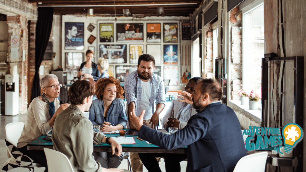 A diverse corporate team participating in a collaborative team building workshop at a rustic indoor venue, led by Adventure Games Inc., with group discussion and problem solving around a shared table.