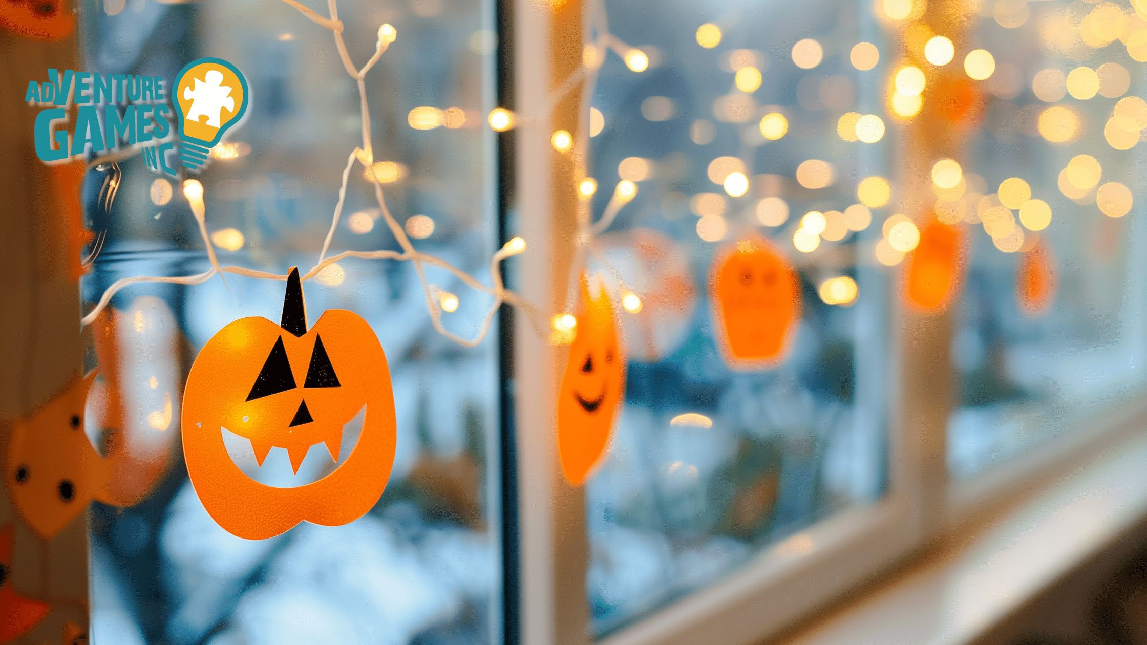 Orange paper jack-o’-lantern string lights glowing along an office window, creating a festive Halloween atmosphere, with blurred background lights and the Adventure Games Inc. logo.