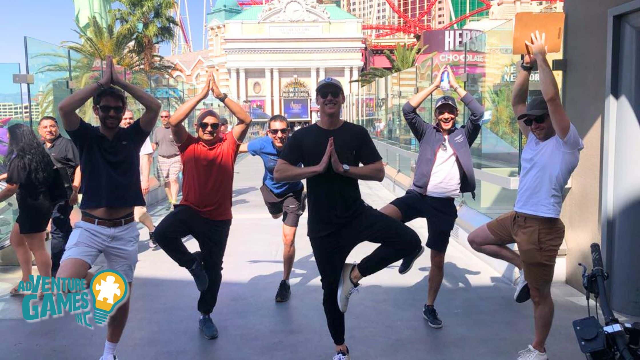A group of coworkers participating in a fun team-building challenge in Las Vegas, striking yoga poses together on the Strip with the New York-New York Hotel & Casino in the background. The team is smiling, engaged, and bonding through the interactive exercise.