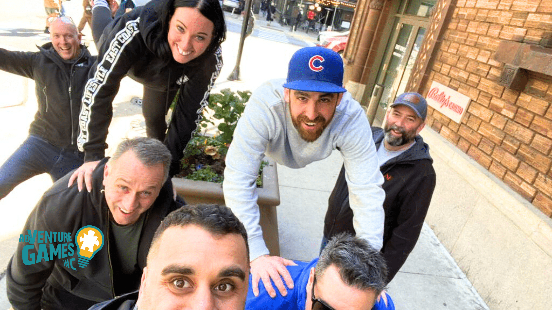 Corporate team building participants forming a human pyramid and smiling during an outdoor challenge by Adventure Games Inc. in a city setting.