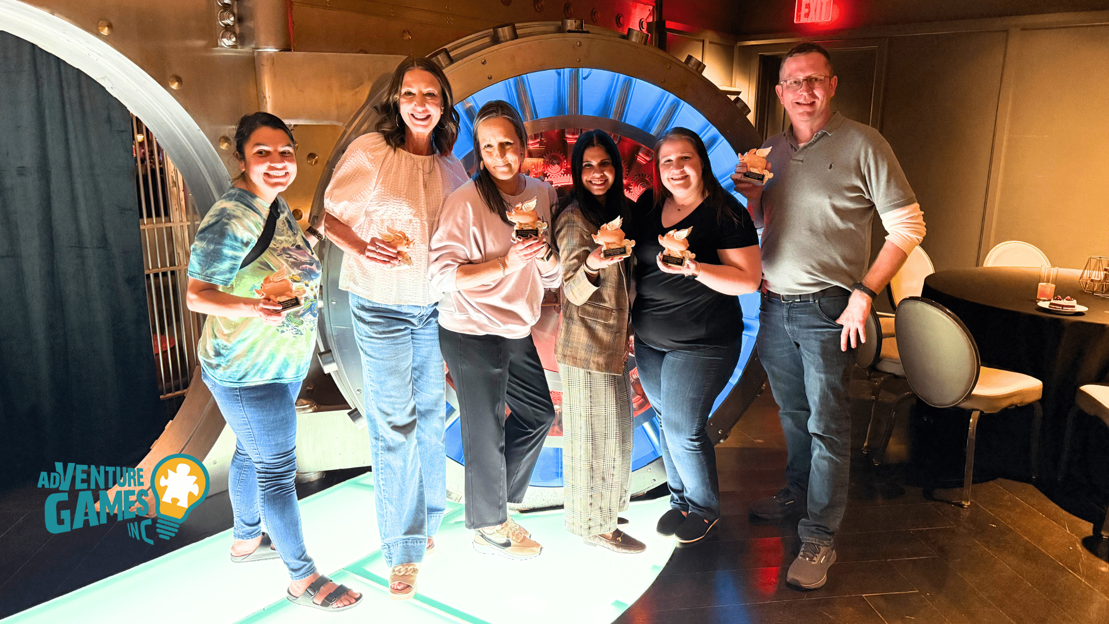 A group of six coworkers celebrating with trophies after completing a corporate team-building challenge hosted by Adventure Games Inc., standing in front of a glowing vault backdrop.