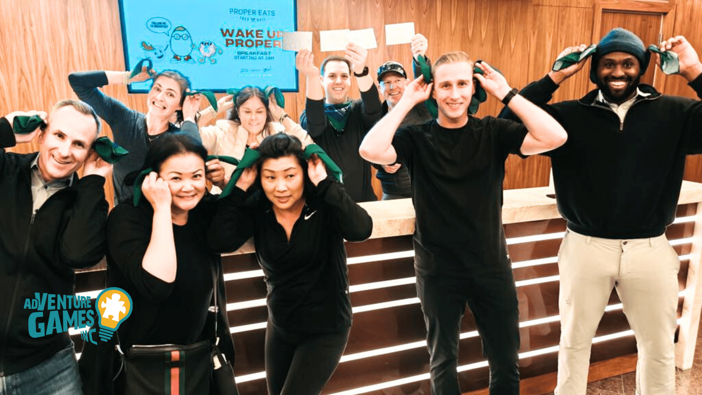 A corporate team smiles and poses with green bandanas during a fun indoor team-building challenge led by Adventure Games Inc.