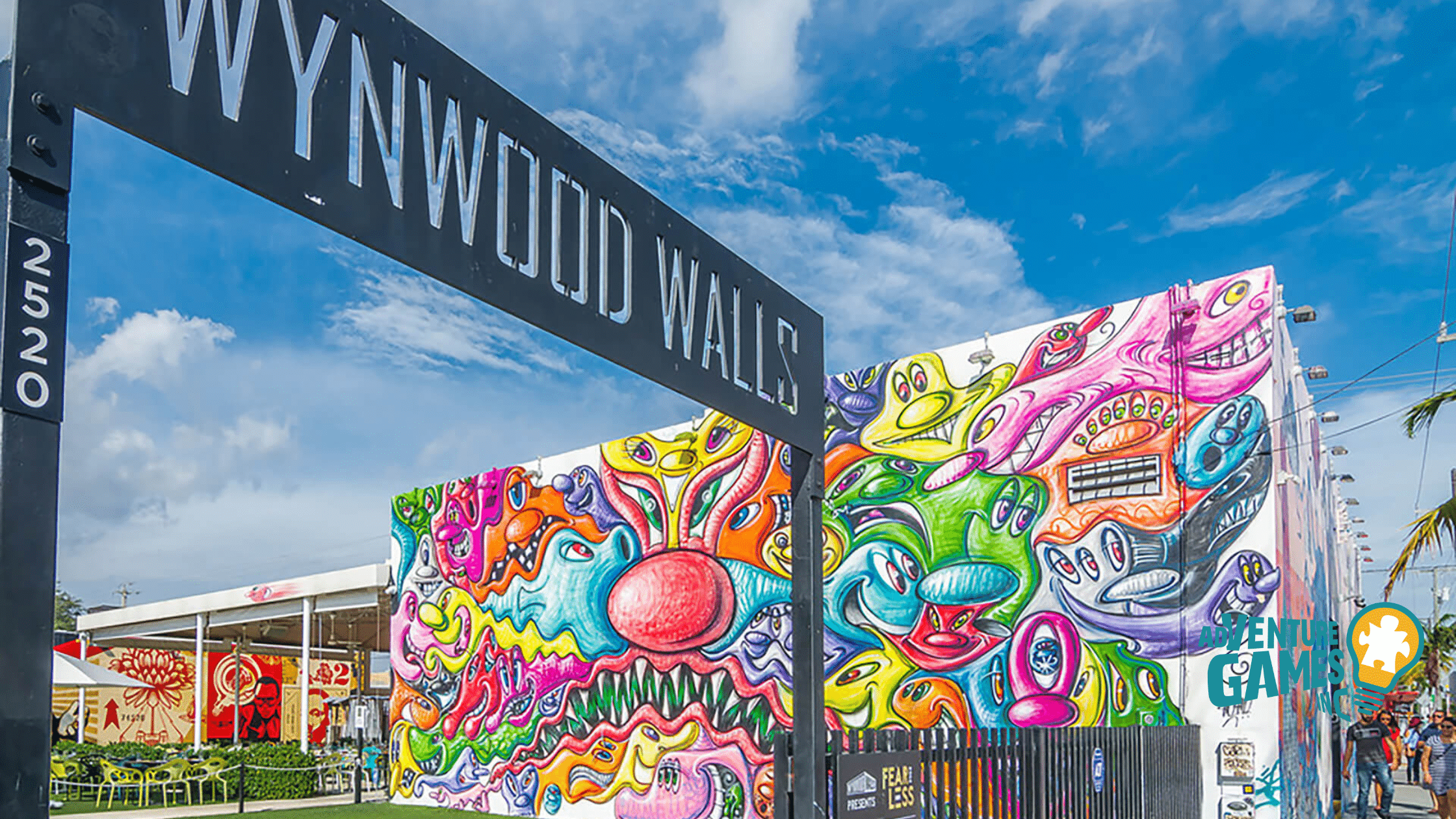 Entrance sign reading “Wynwood Walls” with a vibrant, multicolored abstract mural behind it lining a Miami warehouse wall.