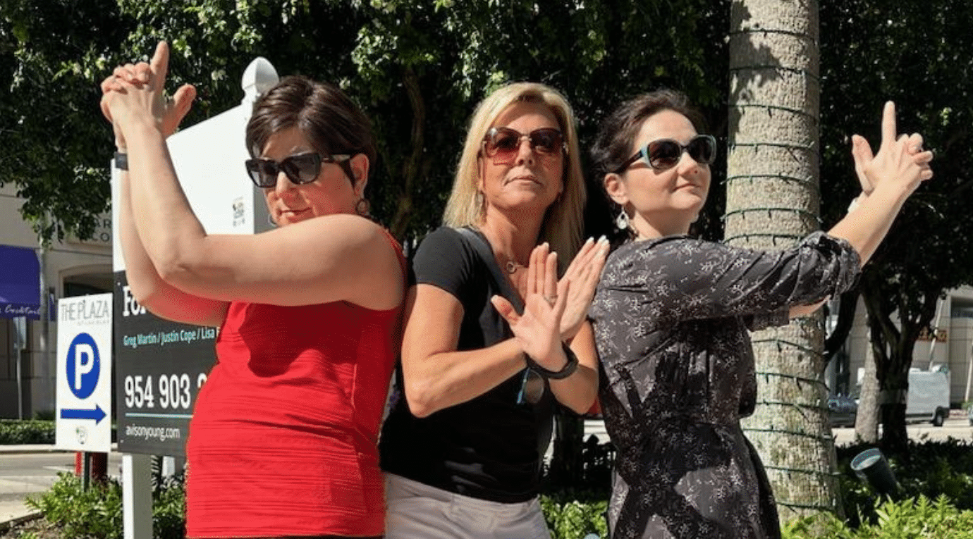 Three coworkers strike playful secret agent poses on a sidewalk during a SpyGame team building challenge led by Adventure Games Inc.