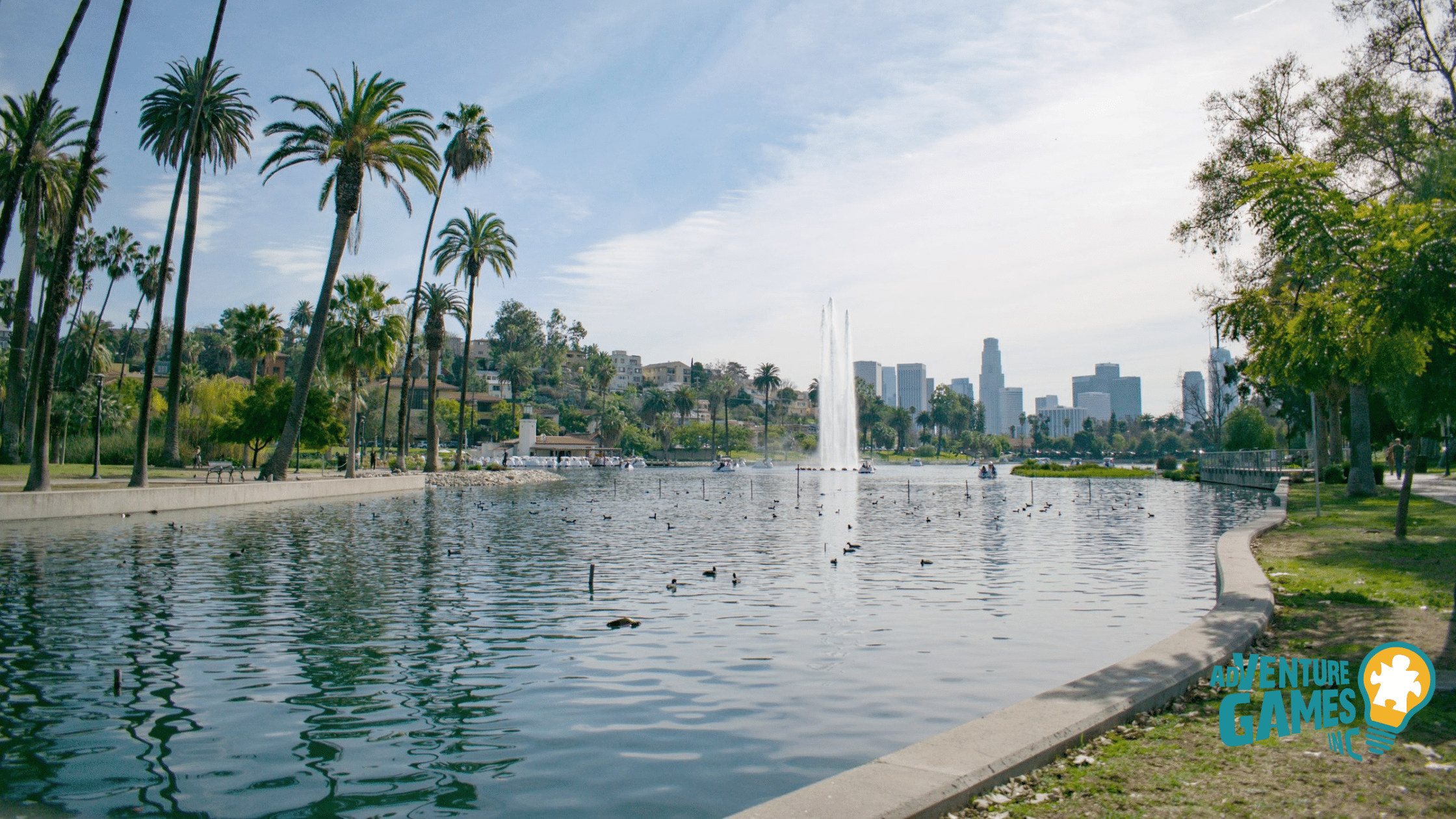 Echo Park Lake in Los Angeles with tall palm trees, a large fountain in the middle of the lake, and downtown skyscrapers in the distance – Adventure Games Inc team building location.