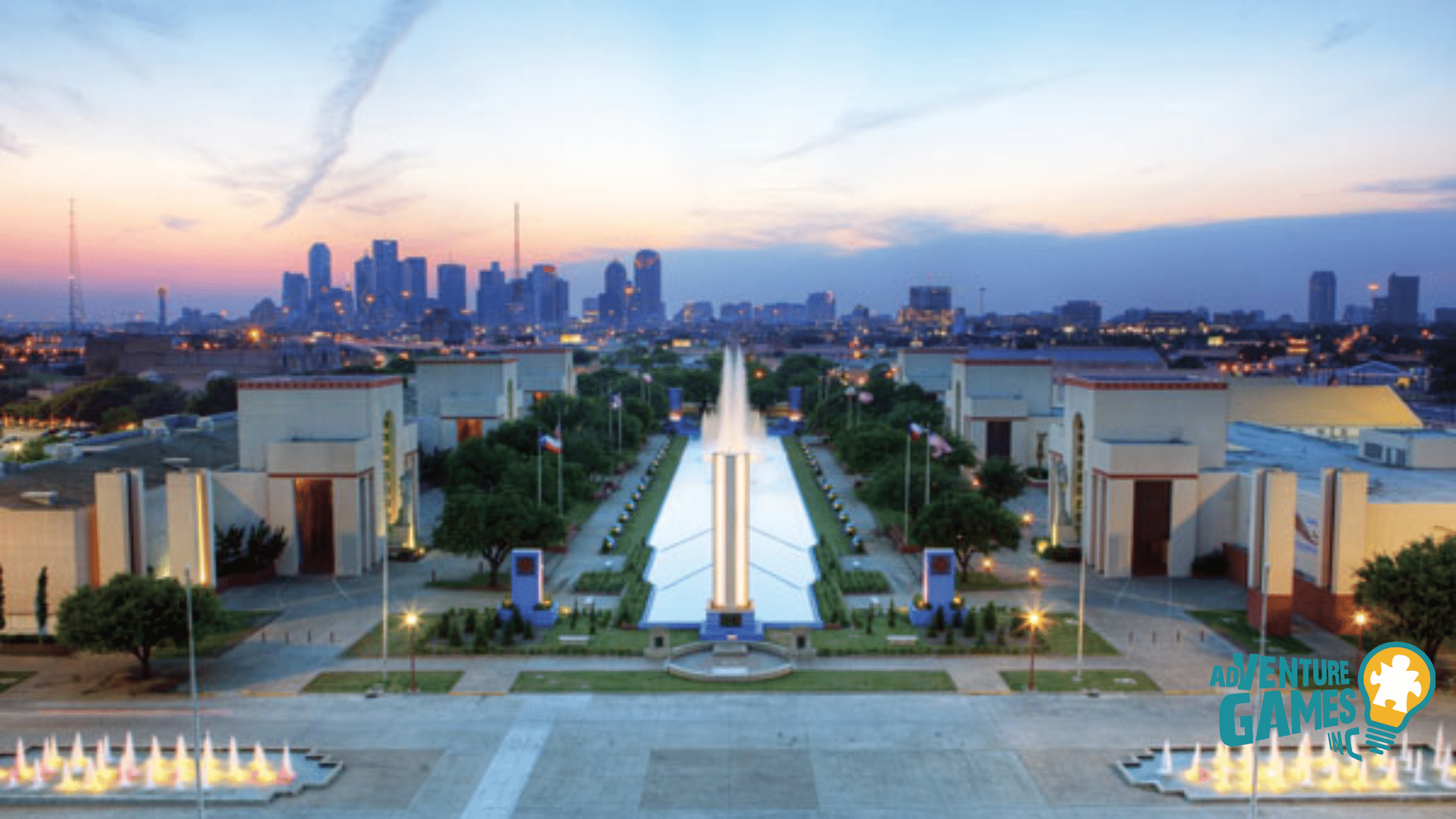 Aerial view of Fair Park at dusk with fountains, Art Deco pavilions and the Dallas skyline, offering spacious grounds for outdoor team building.