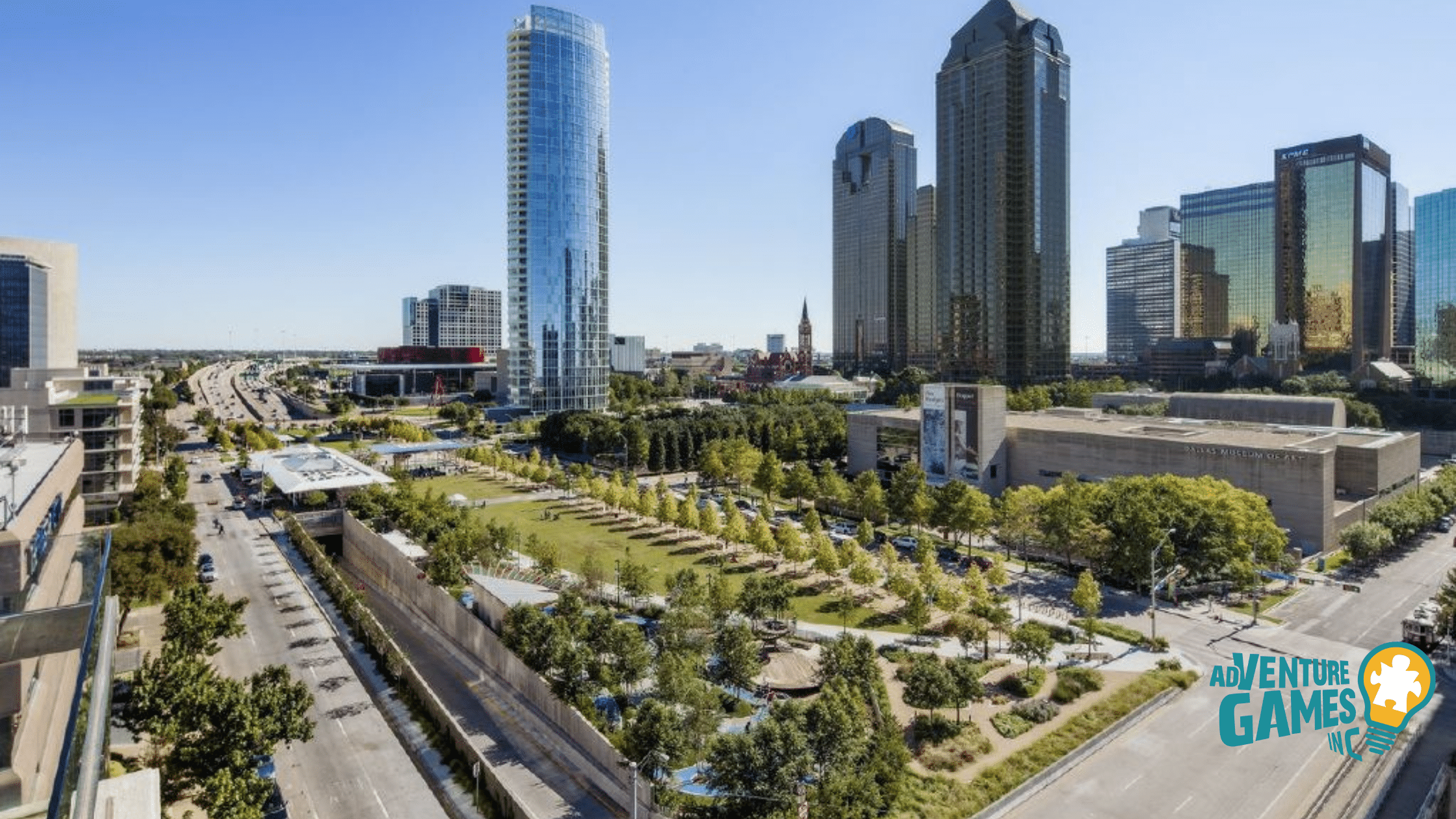 Aerial of Klyde Warren Park with green lawns above the freeway and downtown skyscrapers, a popular location for outdoor team building in Dallas.