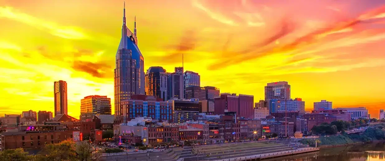 Downtown Nashville skyline at sunset reflected on the Cumberland River, featuring the AT&T ‘Batman’ Building and Riverfront Park.