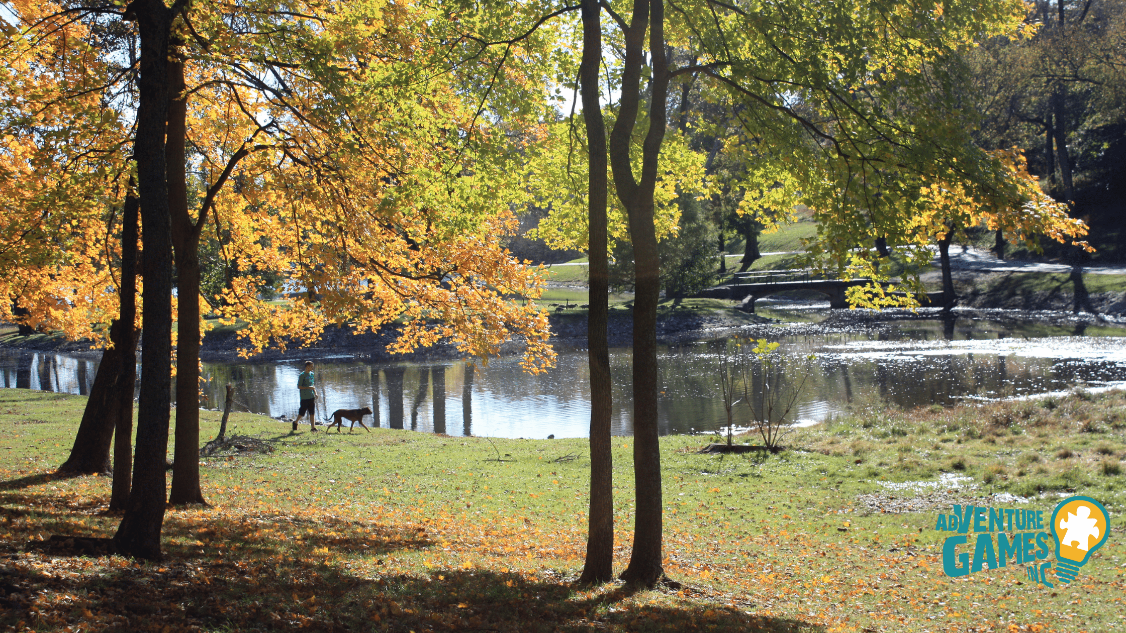 Lakeside trail under autumn trees in Shelby Park with a person walking a dog, East Nashville.