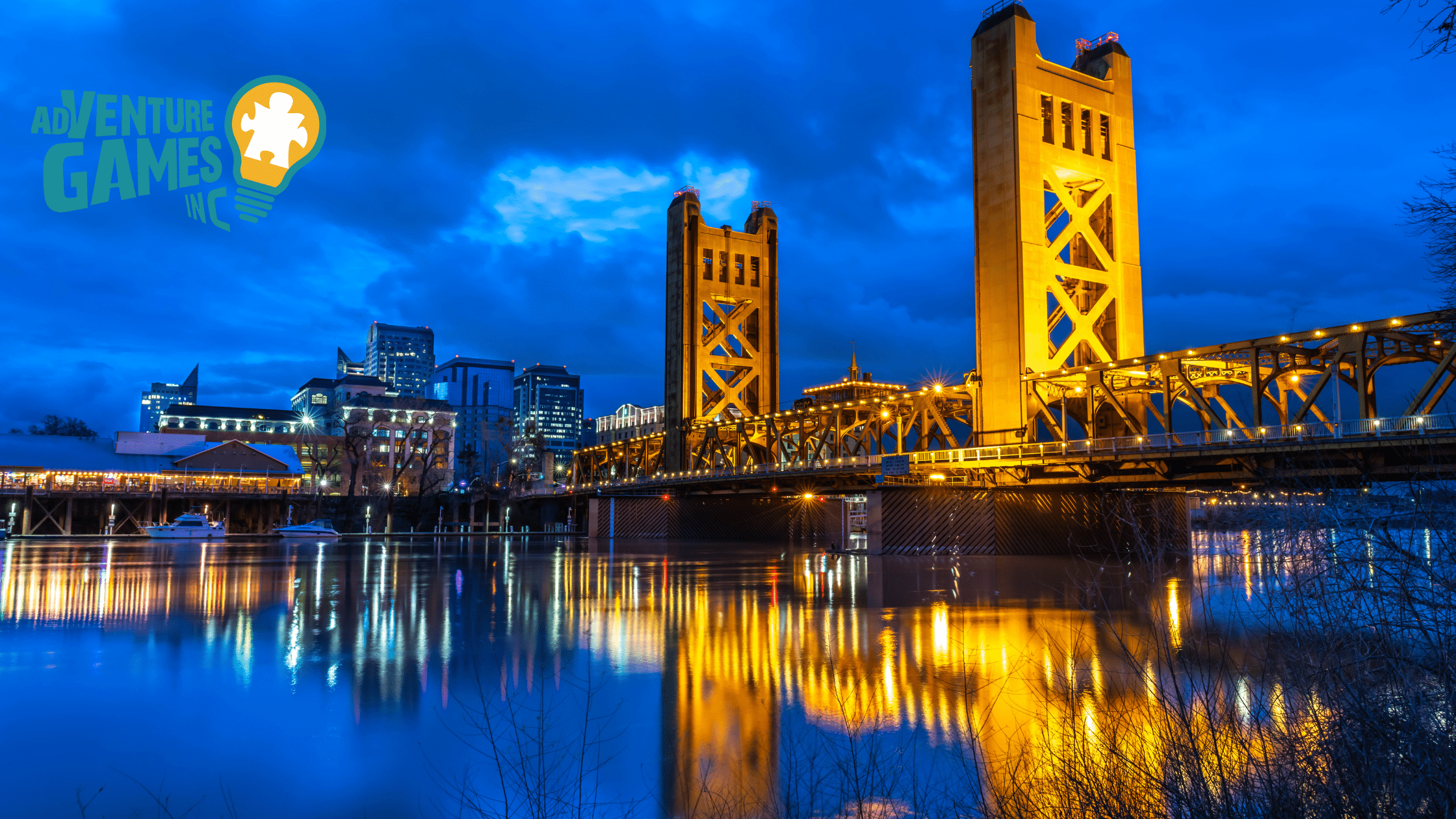 Tower Bridge glowing at night over the Sacramento River, viewed from a riverfront path.