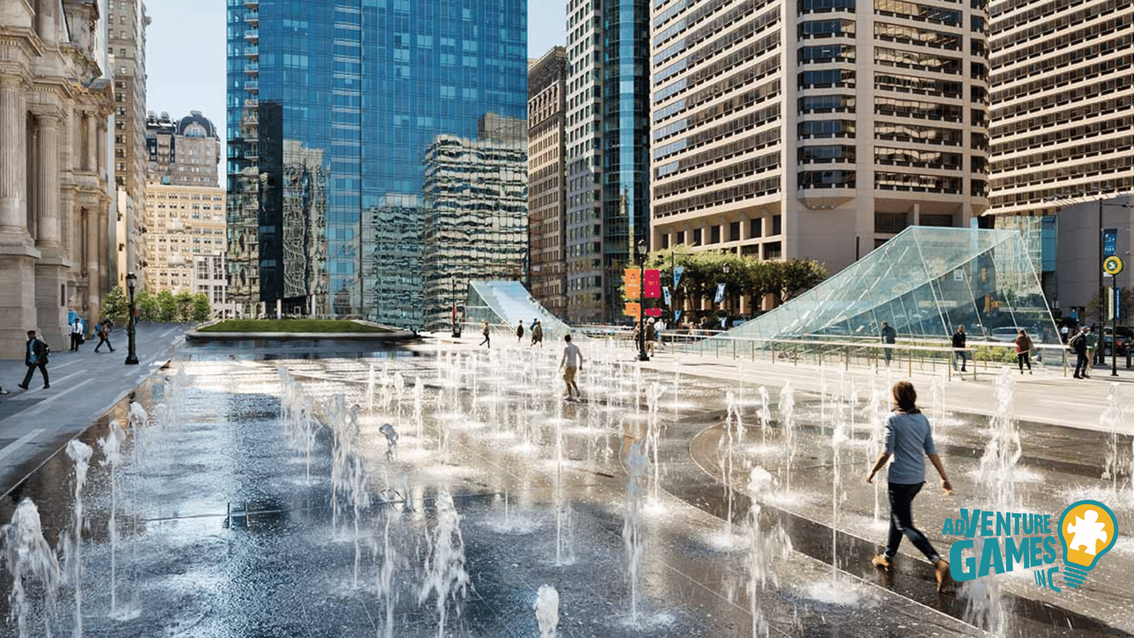 People walking through Dilworth Park’s fountain jets with Philly skyscrapers and glass pavilions—downtown team-building setting.