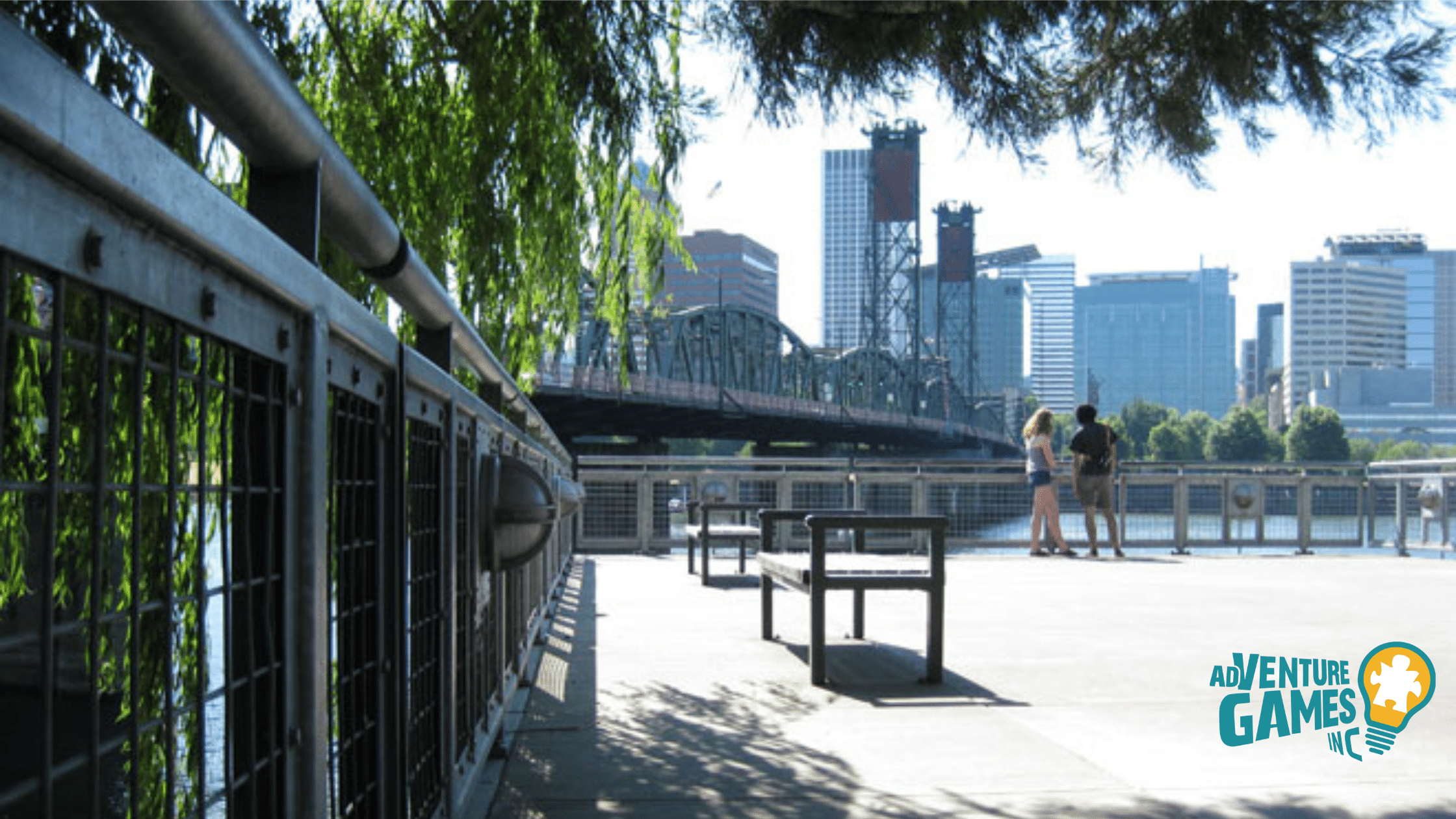 Benches along the Eastbank Esplanade with Portland skyline and steel bridge over the Willamette River.