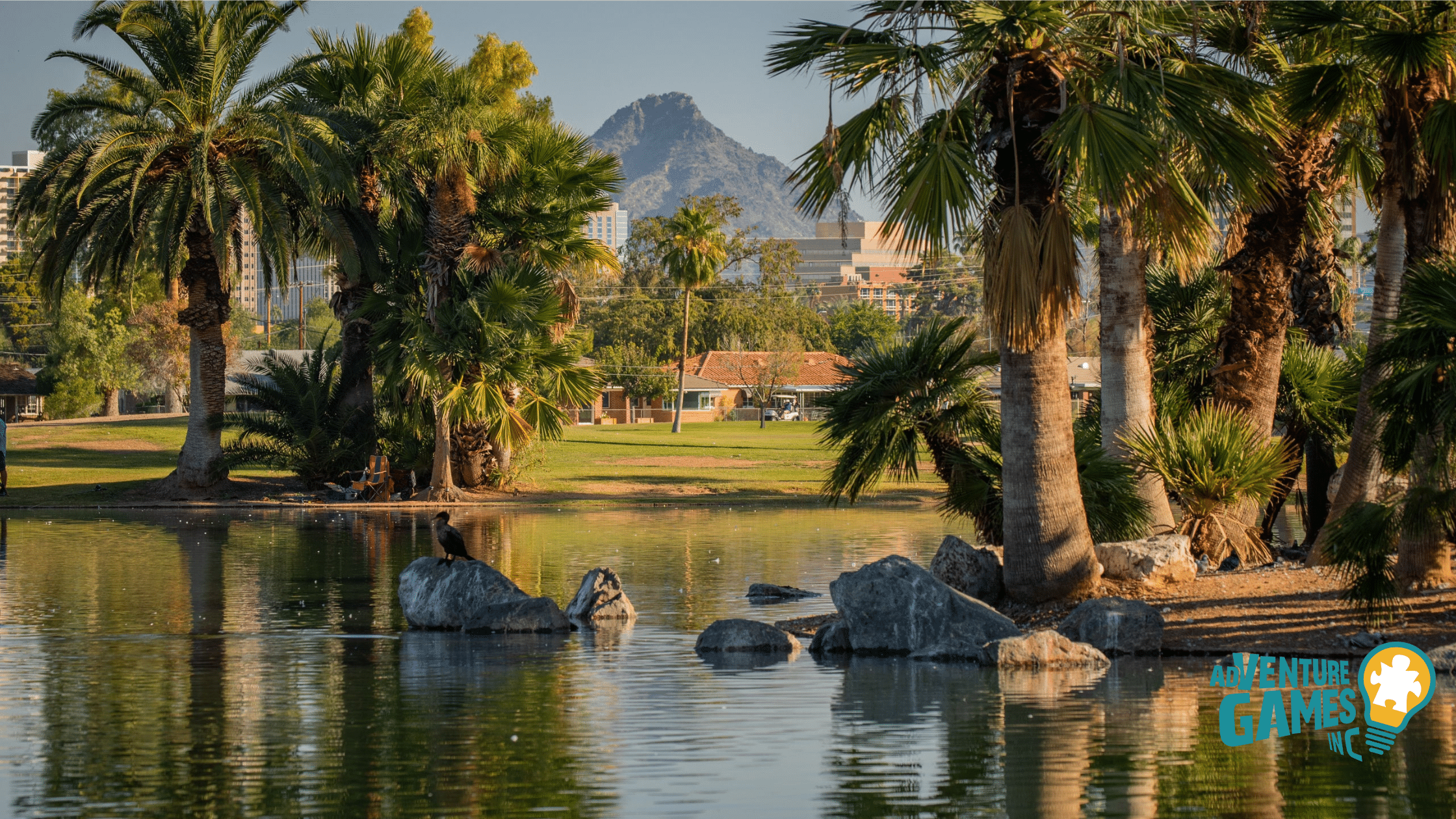 Encanto Park lake framed by palm trees with Phoenix skyline and mountains beyond.