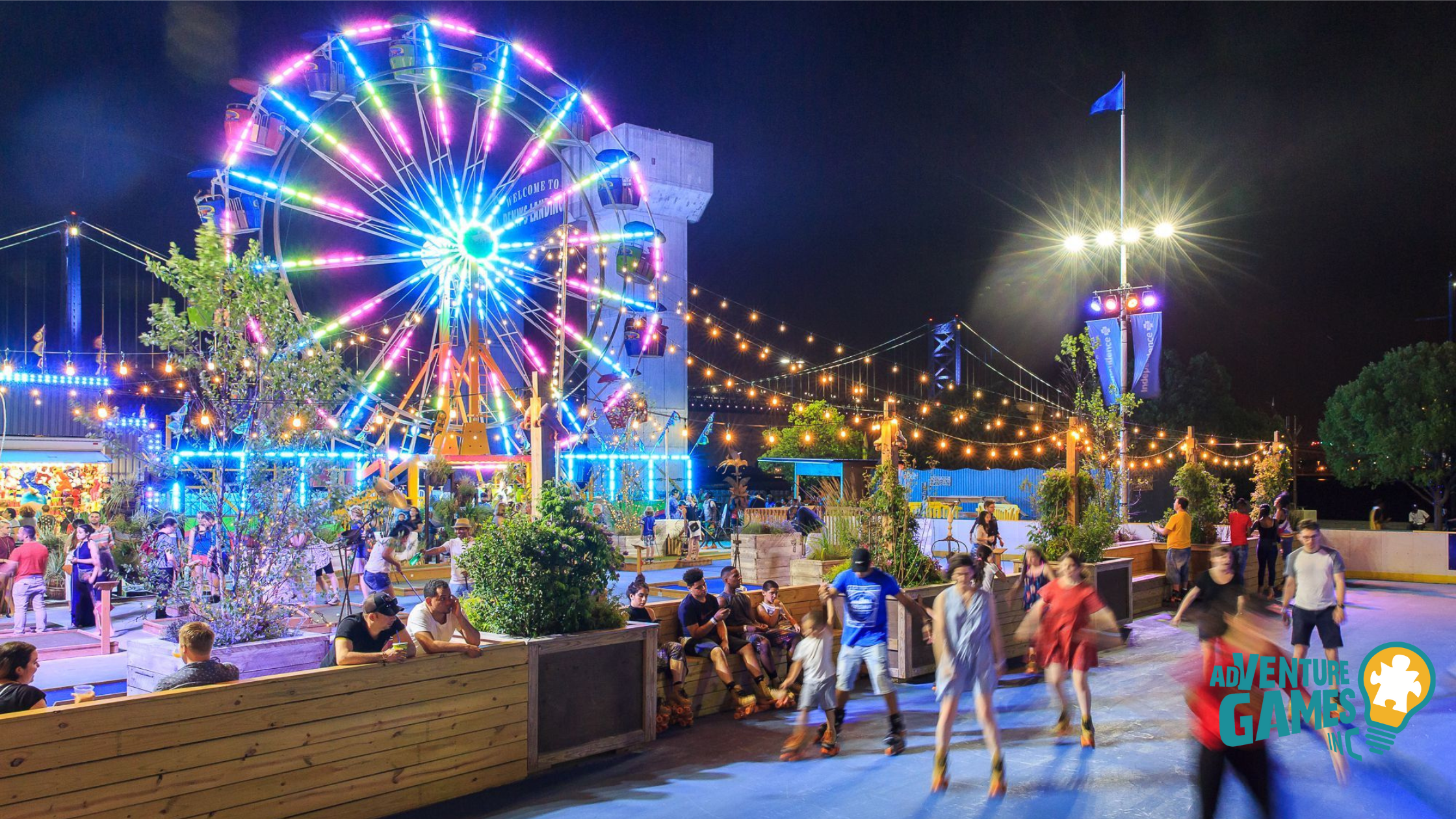 Night scene at Spruce Street Harbor Park with Ferris wheel, string lights, and skaters—festive riverside venue for team fun.