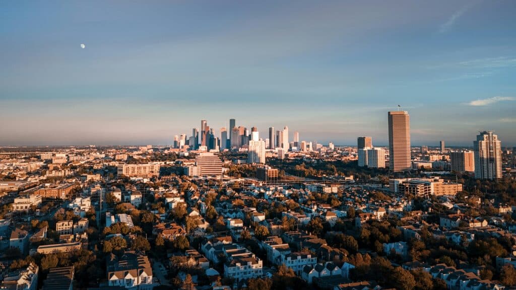Aerial view of the Houston TX skyline at dusk with downtown high-rises and sprawling inner-loop neighborhoods in the foreground