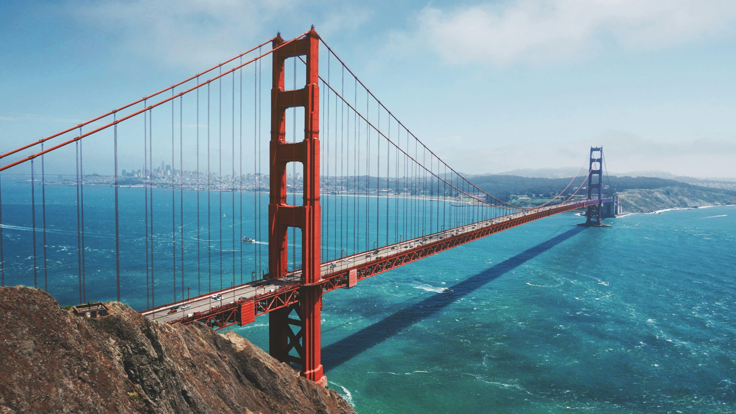 Looking down at the Golden Gate Bridge on a sunny day with light clouds and a beautiful blue sky above.